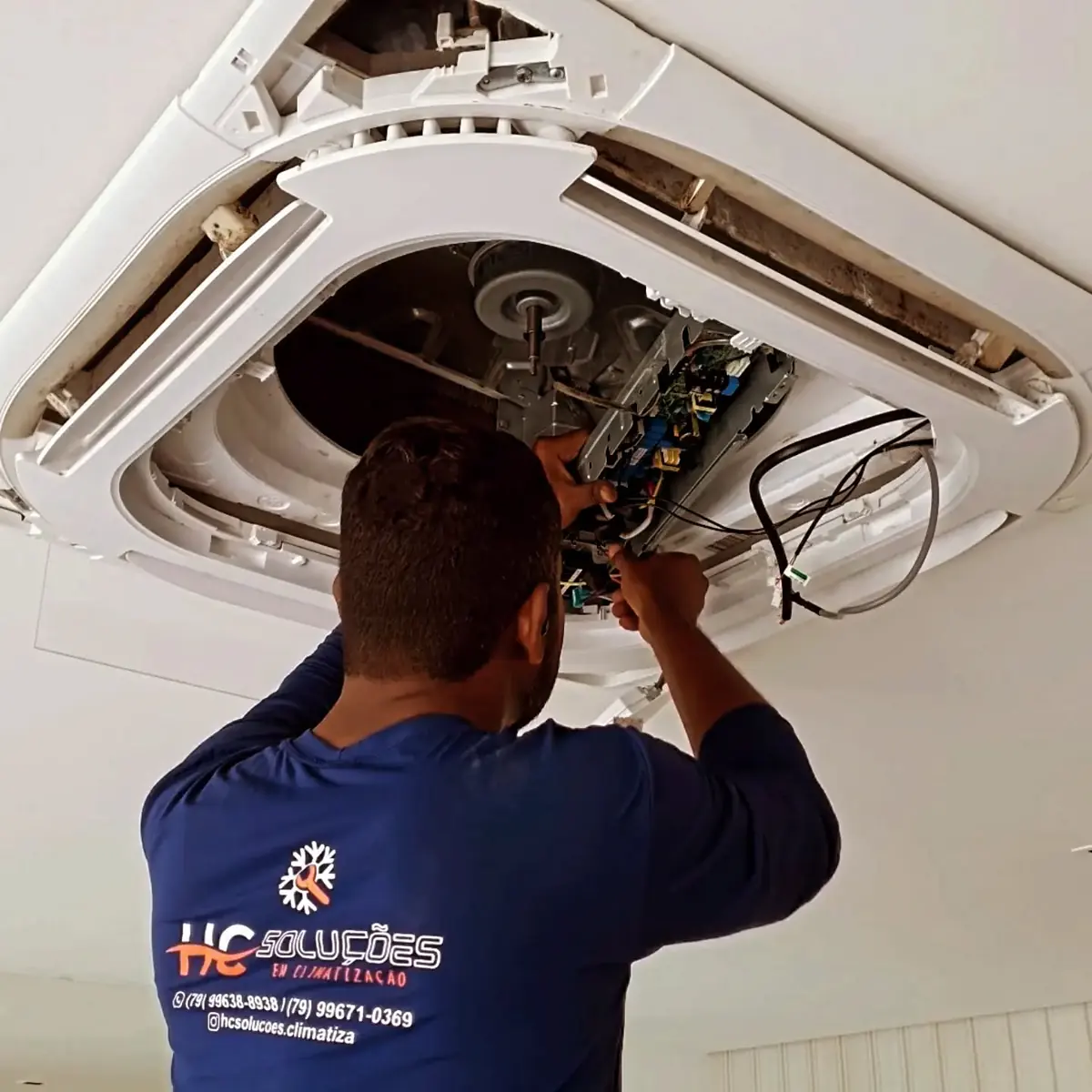 Técnico da HC Soluções de uniforme fazendo manutenção em ar-condicionado cassete