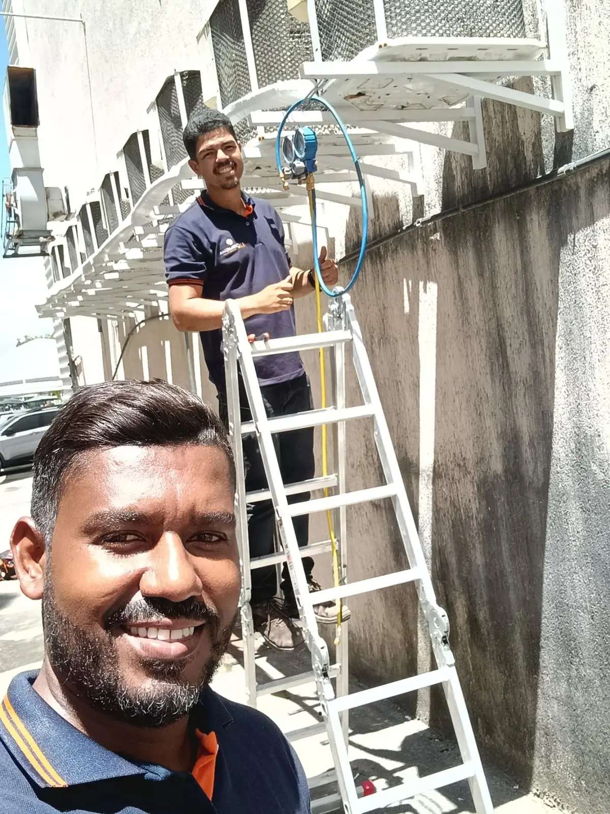 Técnico da HC no alto da escada instalando condensadora em fachada